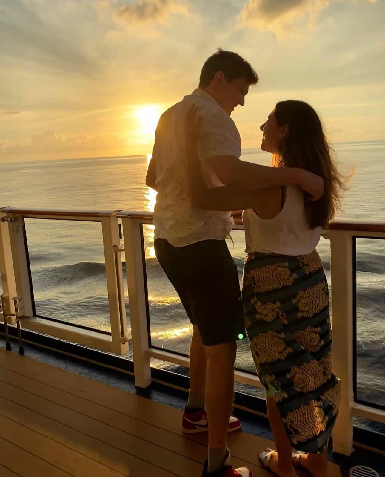 Advisor and a man with their arms around each other on a balcony overlooking the ocean at sunset