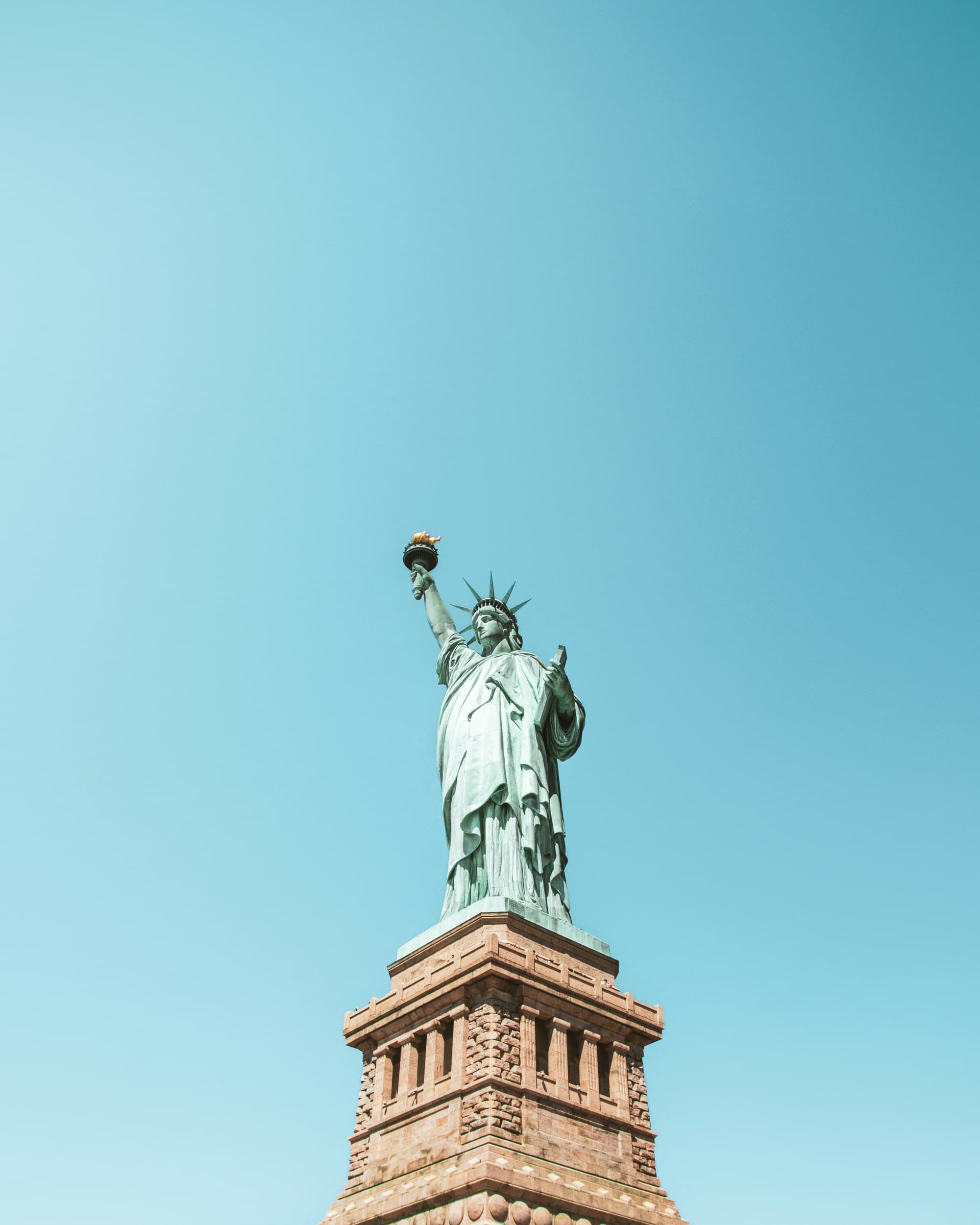A tall, green statue of a woman against a bright blue sky during the daytime
