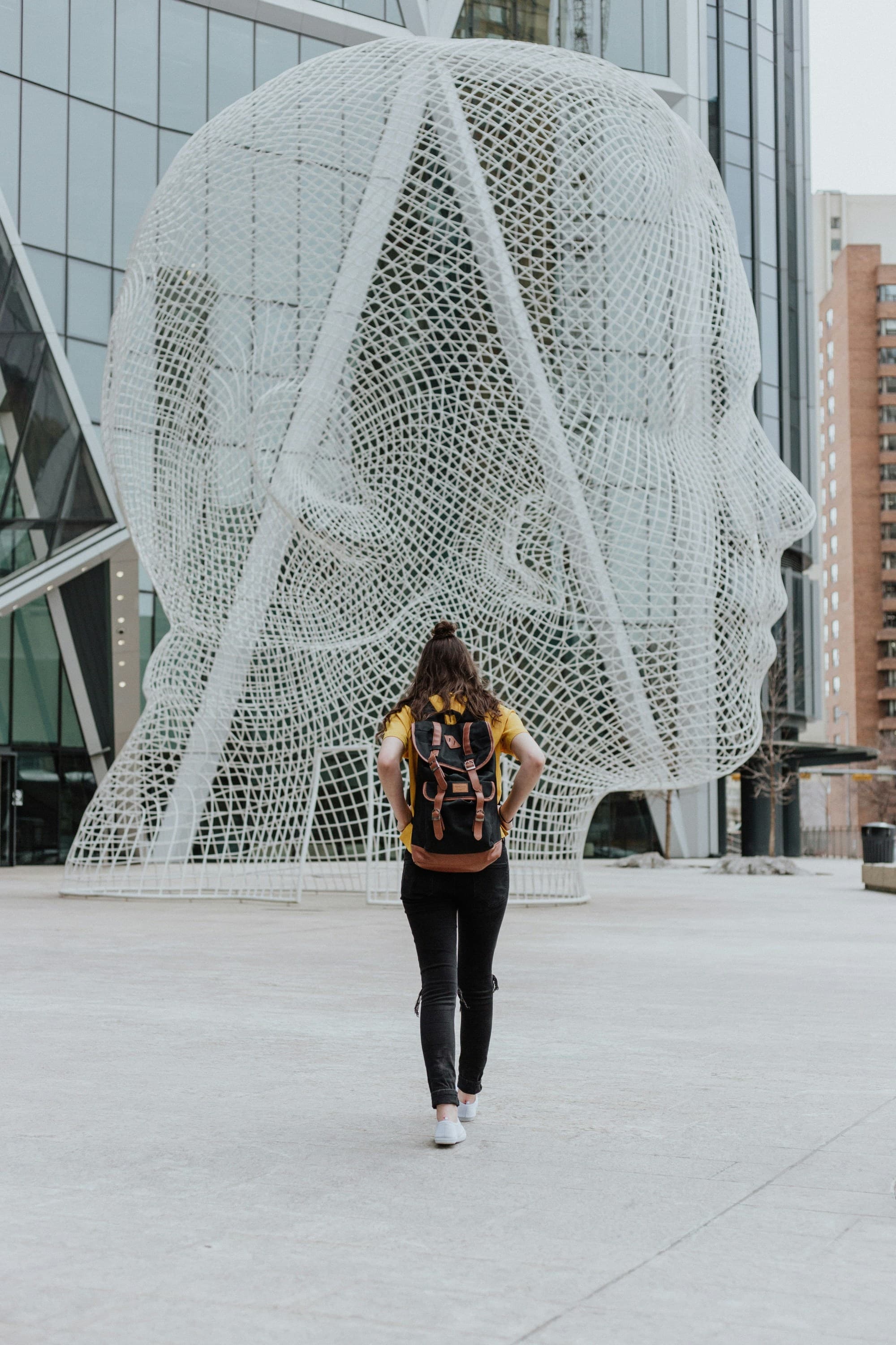 A picture of a girl standing in front of a sculpture in public place.
