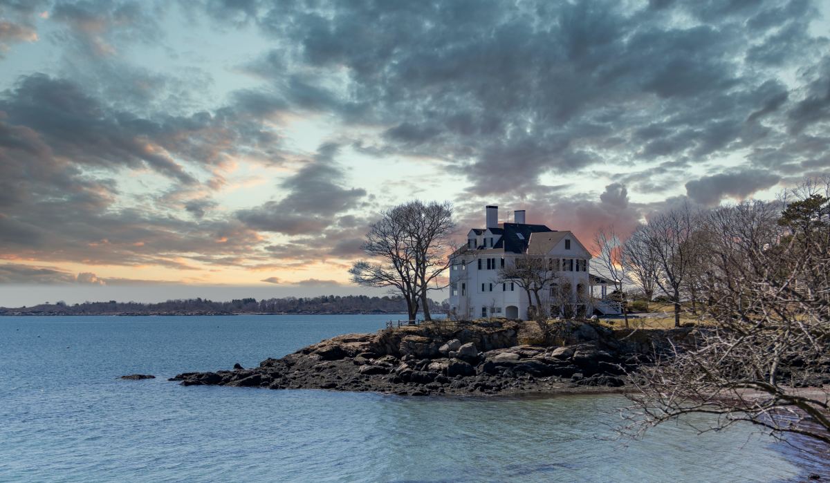 Large white house on the water with a stromy, cloudy sky