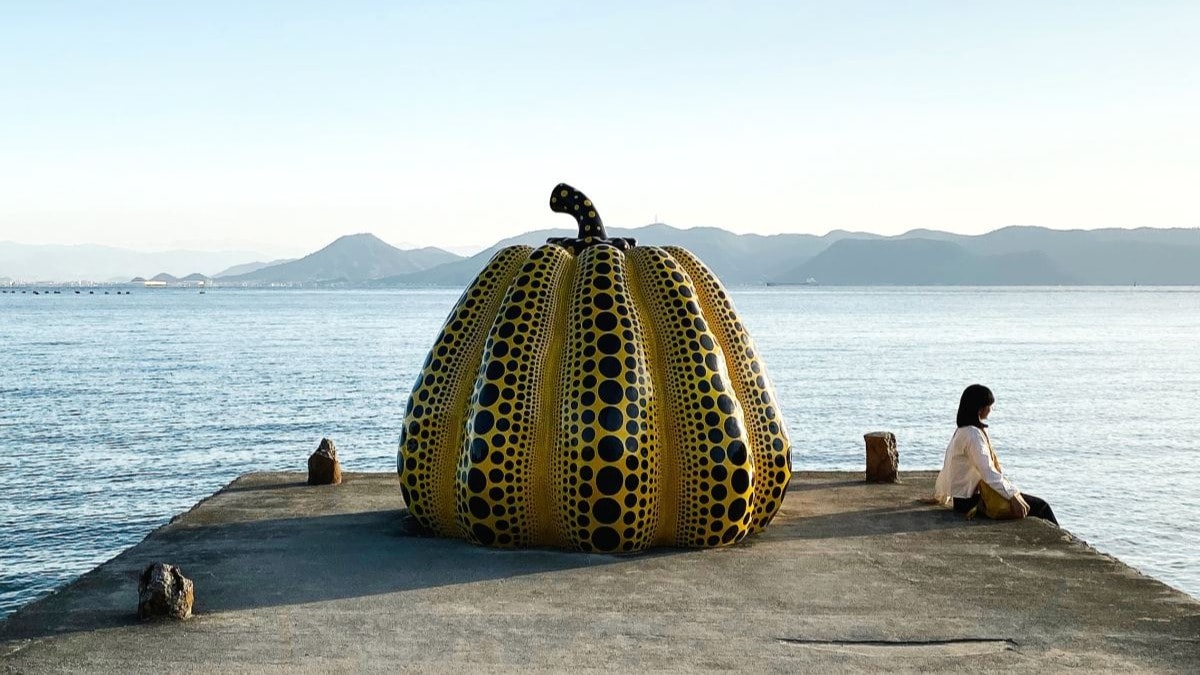 Brown and white pumpkin statue on the edge of a boardwalk on the water.
