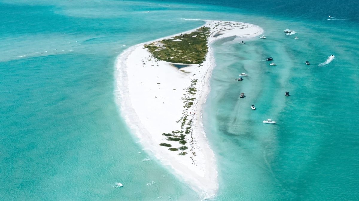 An aerial view of a beach surrounded by bright blue water.