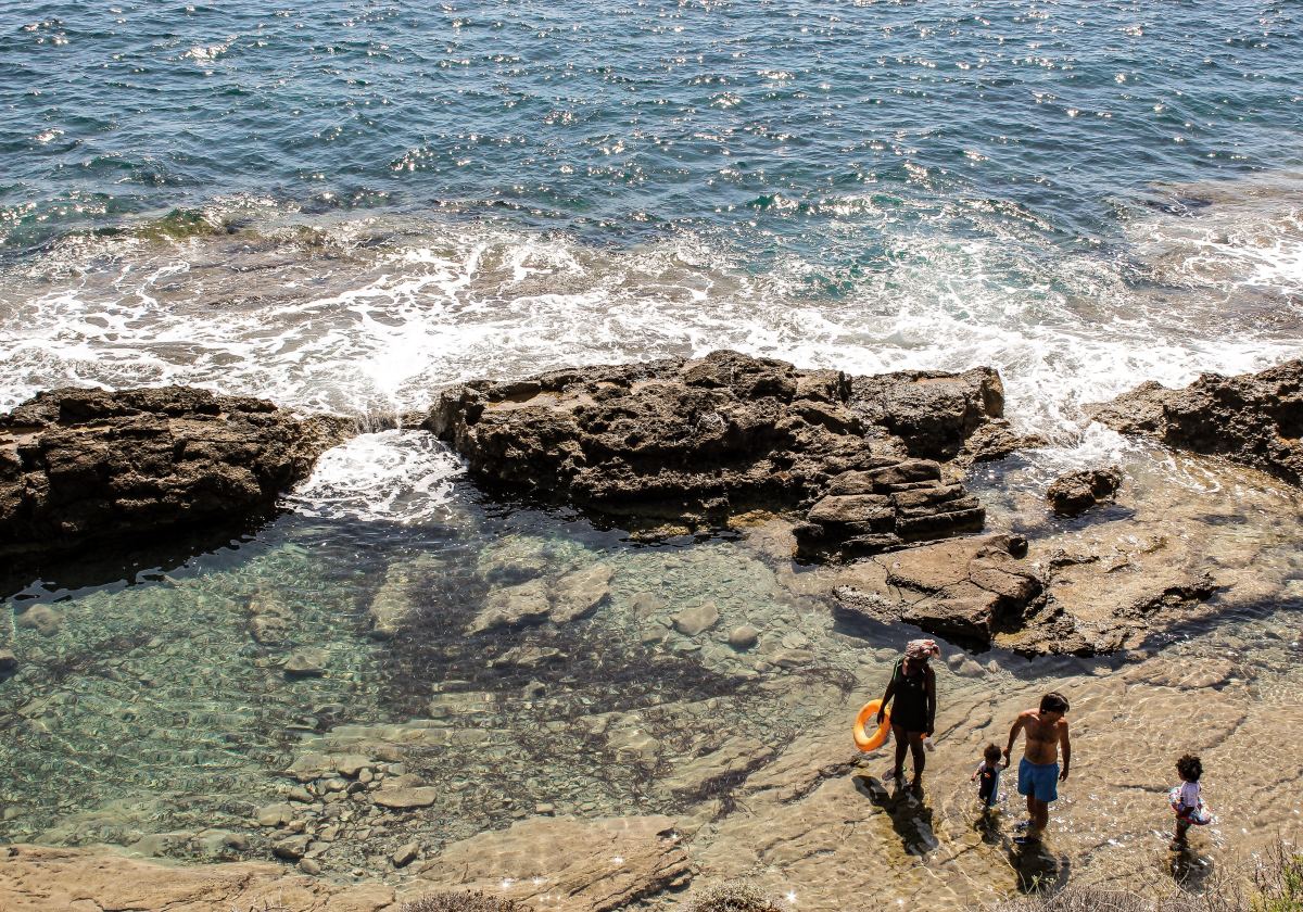 Family near rocks on the beach during daytime.